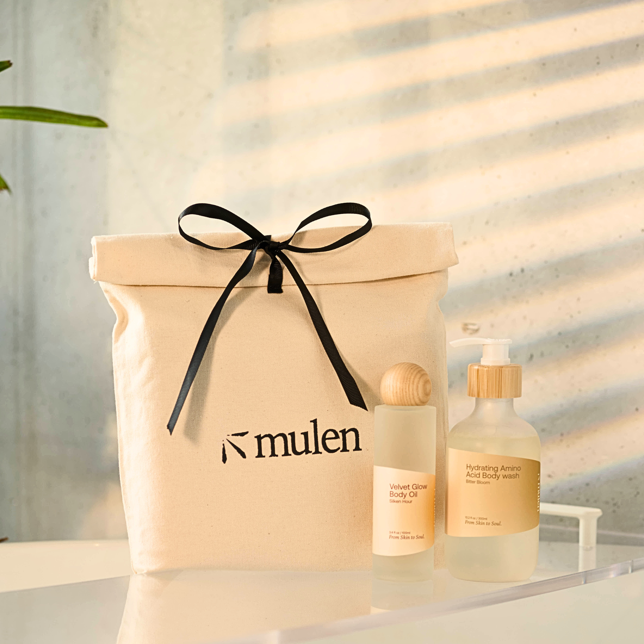Two bottles of body wash and body oil with a beige gift bag featuring the brand 'mulen' on a neutral background.